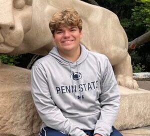 Grayson, diagnosed at 18 with ALK + lung cancer, smiles while wearing a Penn State sweatshirt.