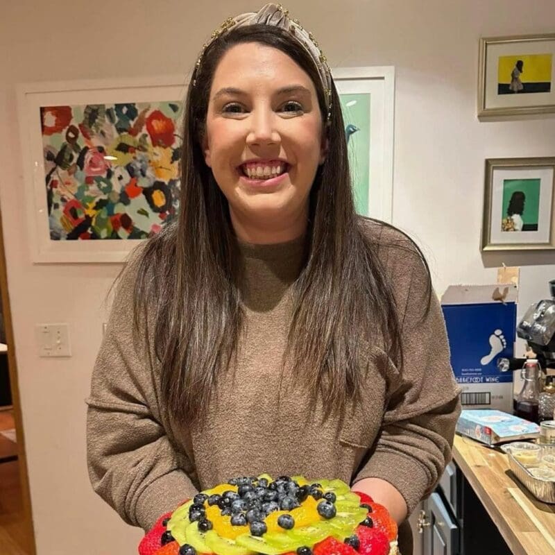 Haley Vermulan was diagnosed with stage IV EGFR NSCLC in 2023 she is a former ER nurse and has 3 children. She is smiling holding fruit wearing a brown sweater with brown hair.