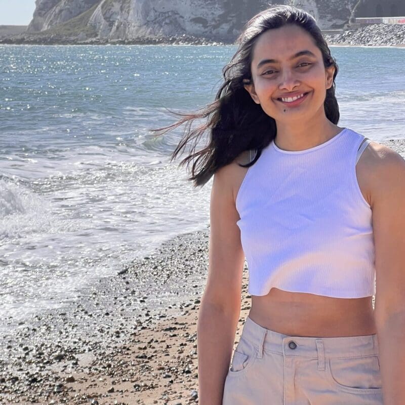 Rasika, a young woman from India with lung cancer, smiles on a beach.