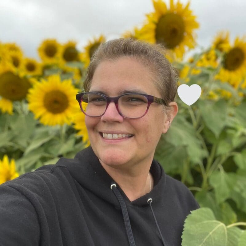 Theresa Woodbury, diagnosed with stage 4 EGFR lung cancer, smiles in a field of sunflowers. In loving memory.