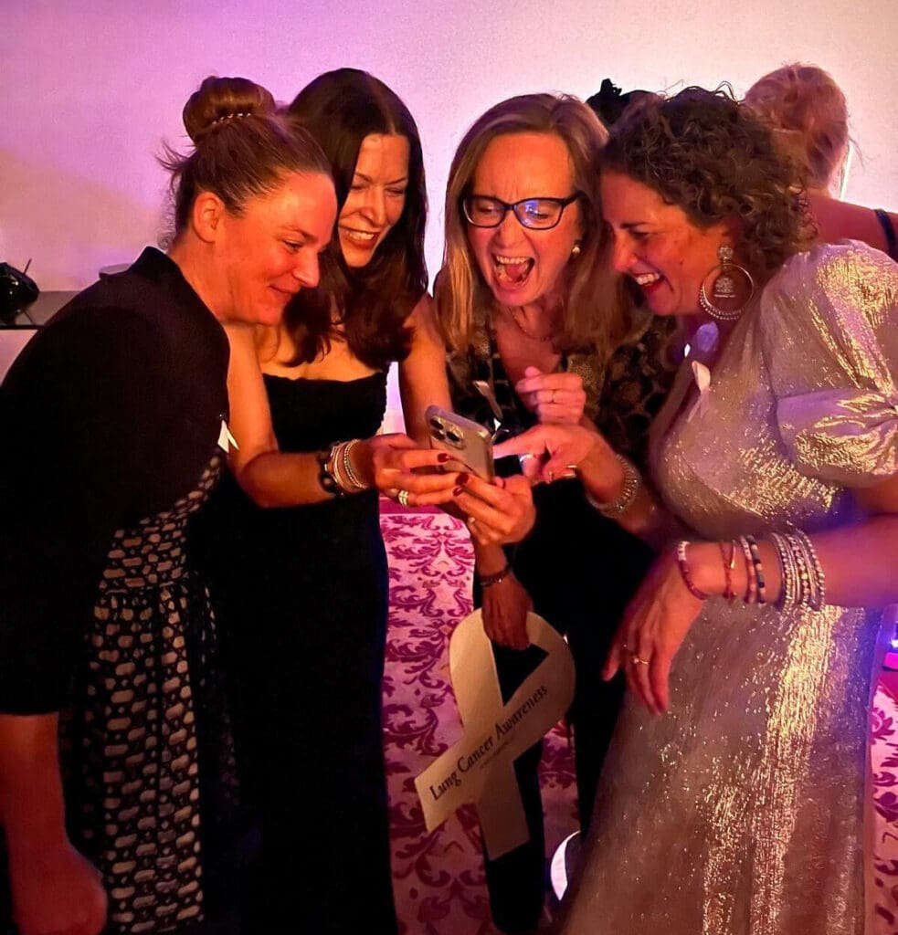A group of lung cancer patients in formal gowns laughing together at a Oncogene Cancer Research event