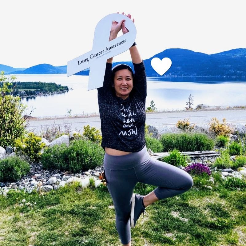 Adrienne, a young lung cancer patient in a yoga post holding a lung cancer awareness white ribbon