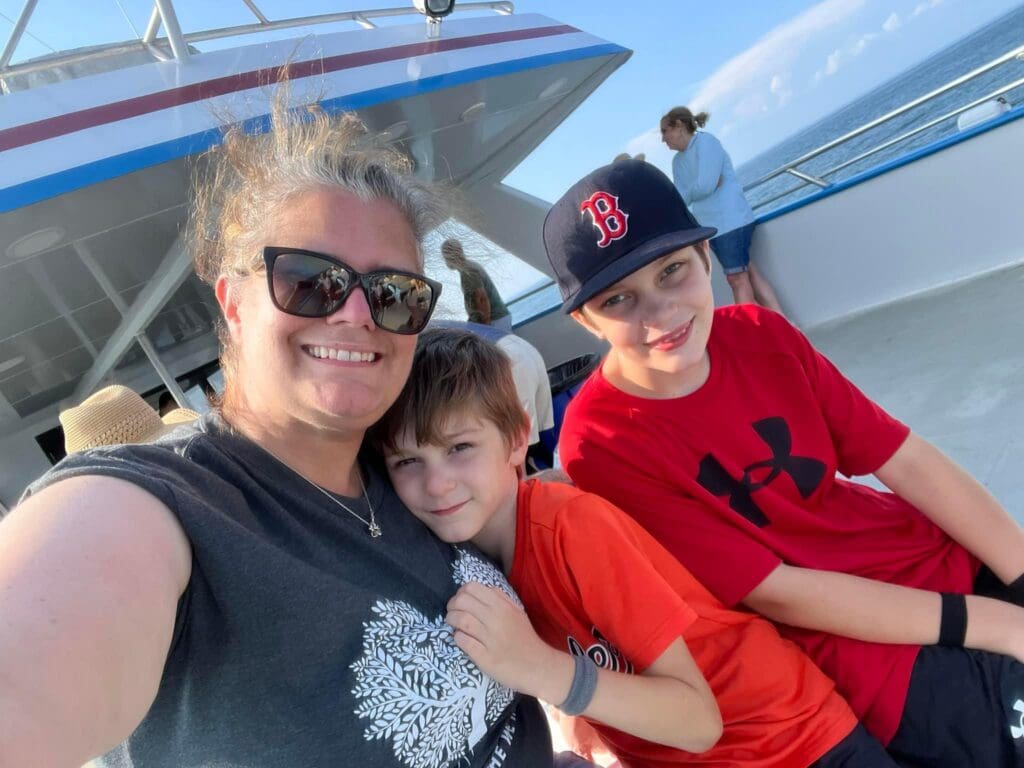 Theresa Woodbury smiling with her two sons on a boat on a sunny day.
