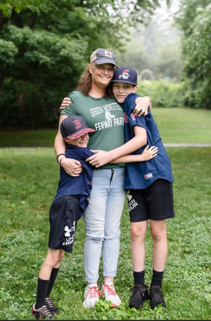Theresa and her sons hugging together outdoors on a grassy lawn