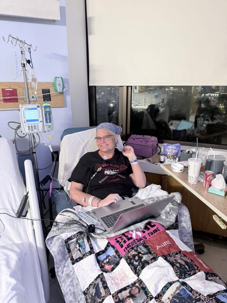 Theresa Woodbury, a lung cancer patient, smiling and working on her laptop in a hospital bed.