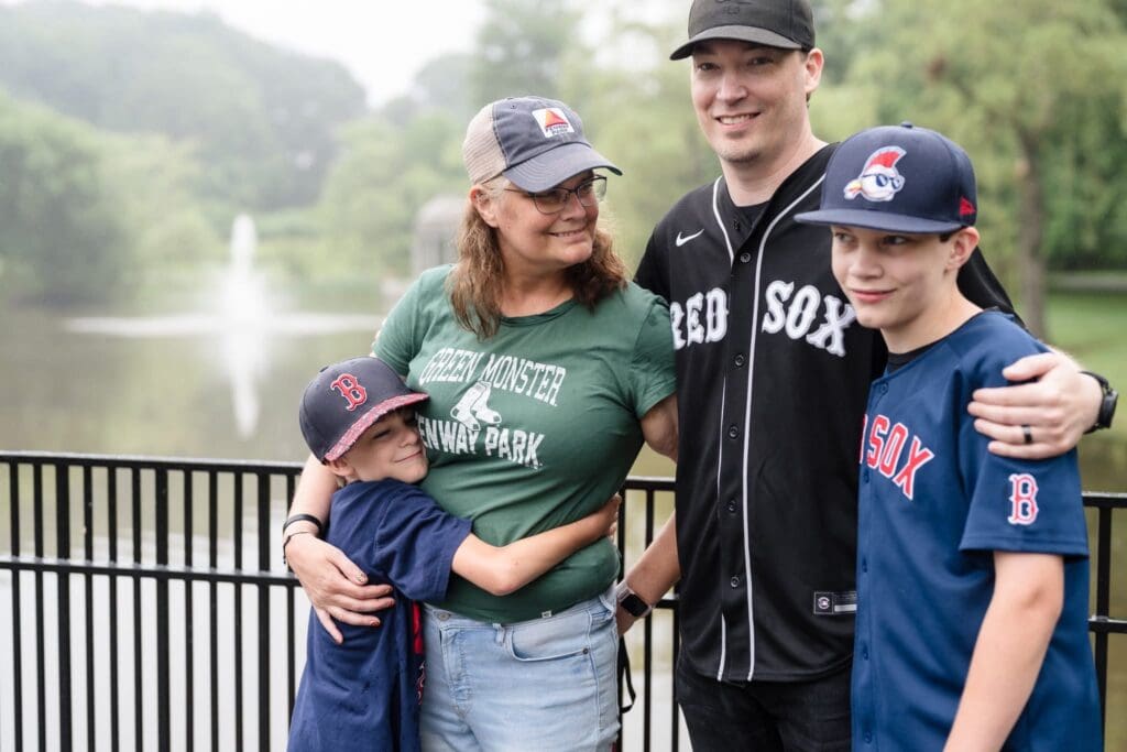 Theresa Woodbury smiling with her husband and two sons, all wearing Red Sox jerseys.