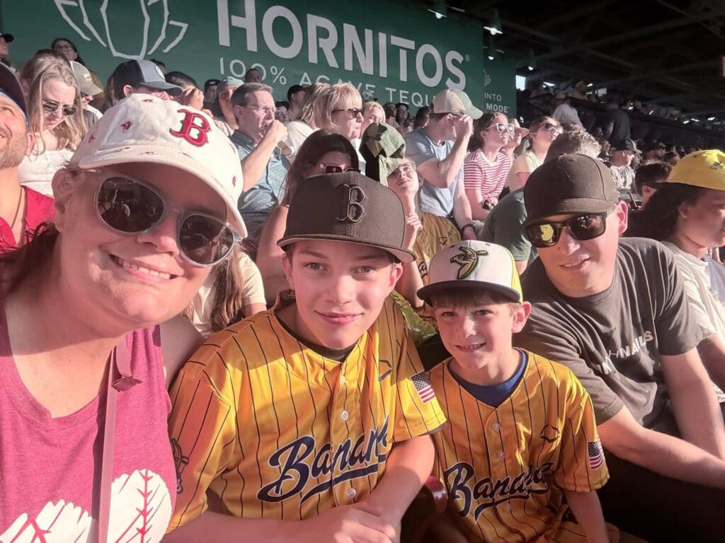 Theresa and her two boys, and her husband one in a Savannah Bananas jersey, at a sporting event