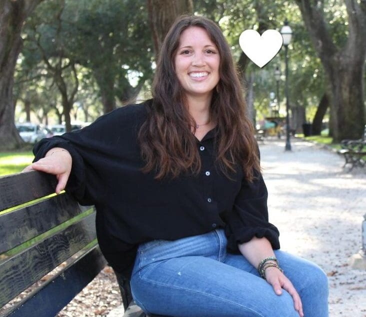 Kelly, a young patient with lung cancer, smiles outdoors in a tree-lined park.