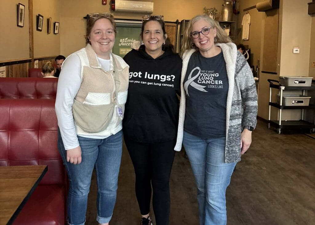 Juliet, Loryn, and Jen, young lung cancer community members, smiling together at a restaurant.