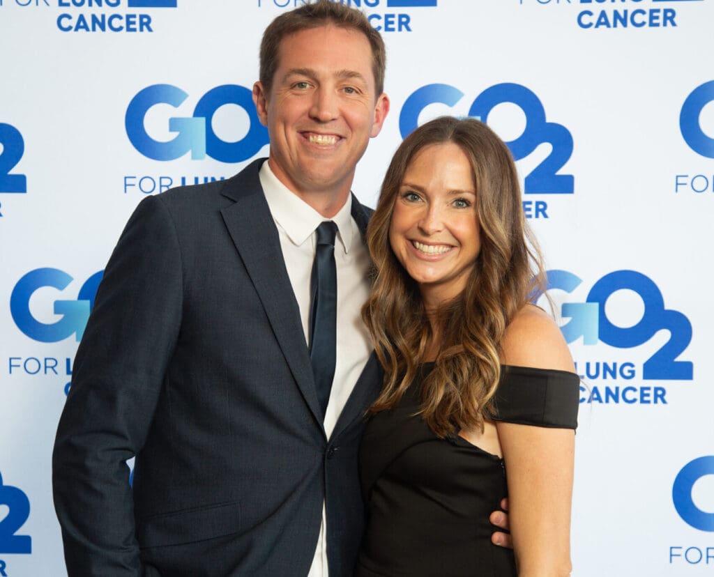 Emily, a long term stage 4 lung cancer survivor, smiles with her husband at a go2 for lung cancer gala