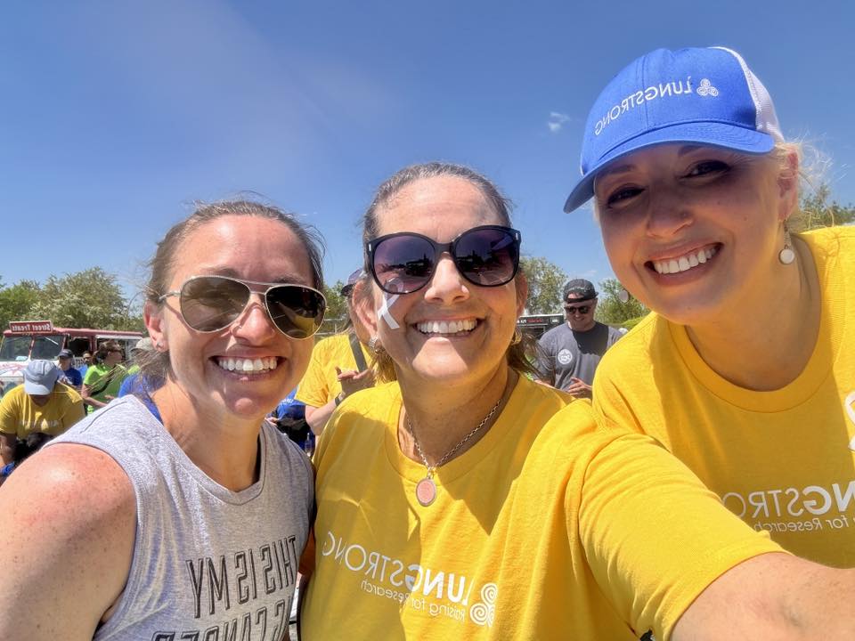 Three young lung cancer patients wearing yellow lungforce shirts smile together at a community lung cancer walk