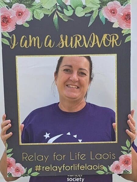 A young lung cancer patient, Samantha, smiling holding a "I am a survivor" sign