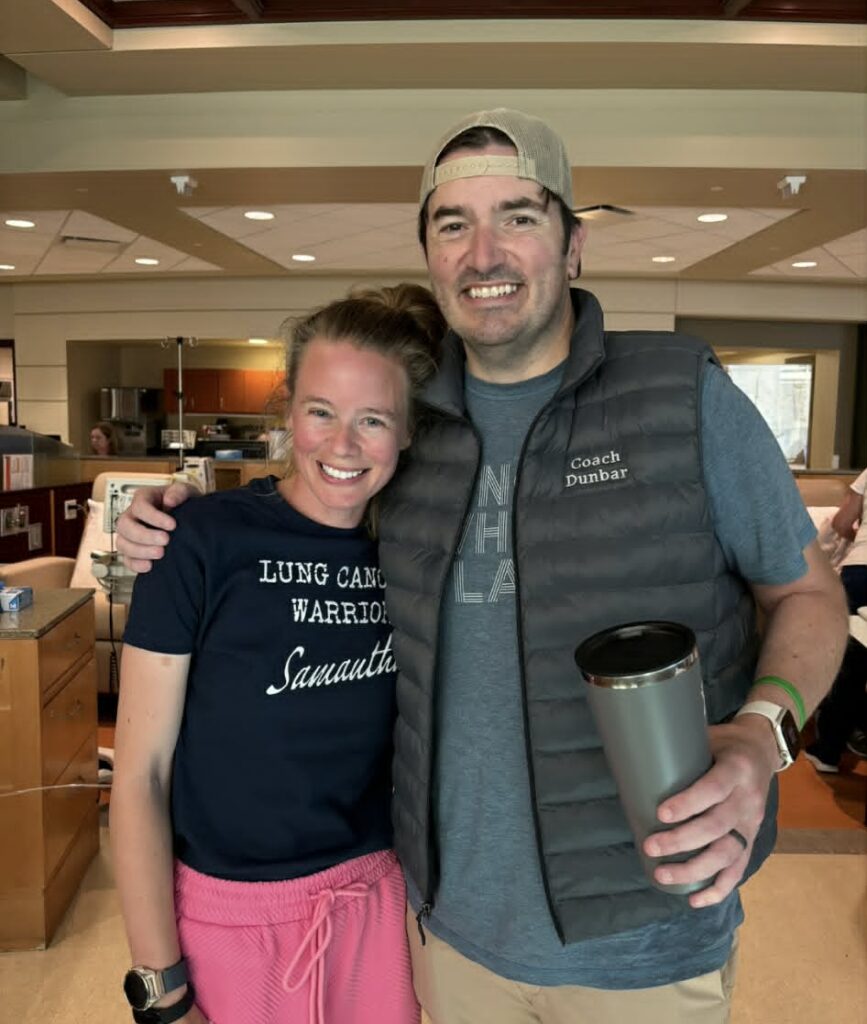 Samantha and Chad, two young lung cancer patients smile during Samantha's infusion treatment. Samantha is wearing a "lung cancer warrior" shirt