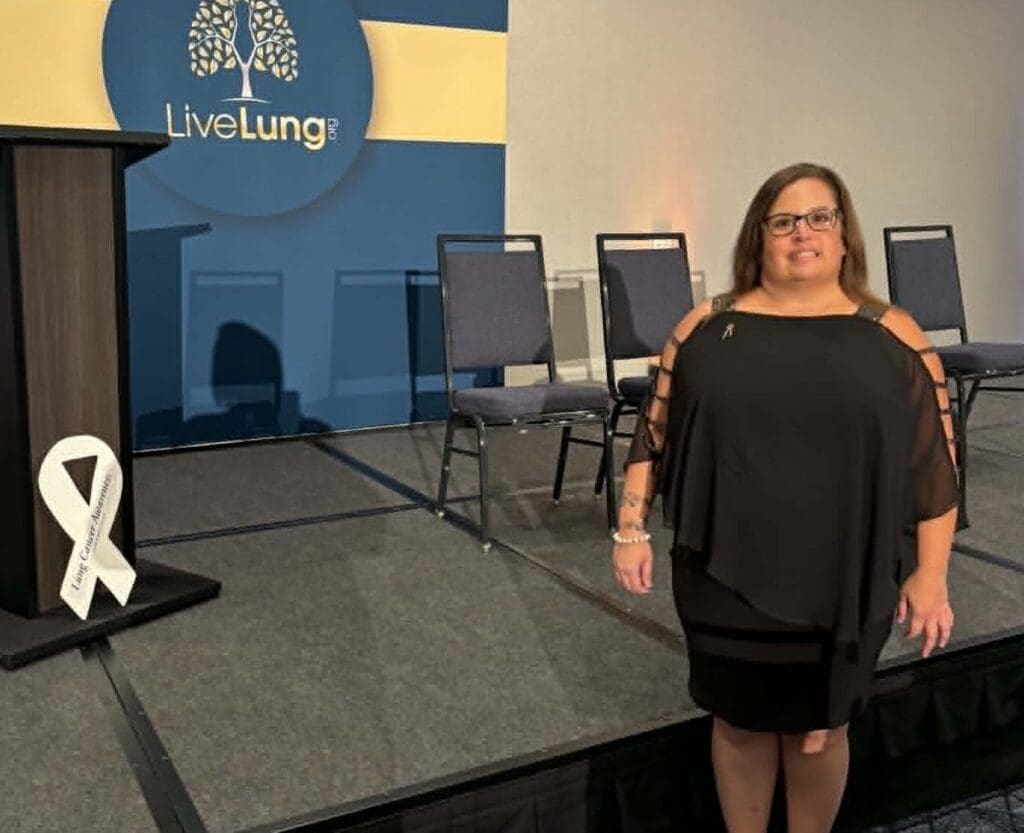 Tiffany, a young lung cancer patient, standing beside a LiveLung event stage backdrop
