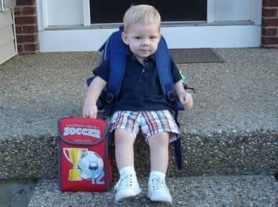 Leah’s young son sitting on the front steps with his backpack and lunchbox