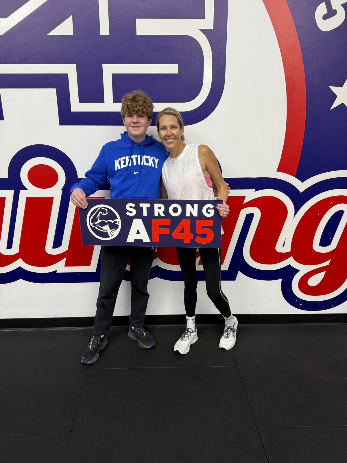 Leah and her son at an F45 gym holding a Strong AF45 sign